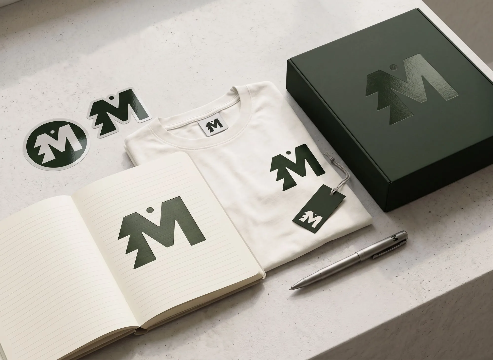 MAGZ branding applied to a notebook, folded t-shirt with woven label and hang tag, stickers, a pen and a gift box — all in forest green on cream